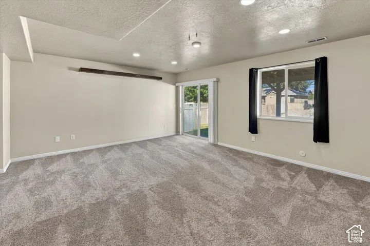 Neutral-toned interior featuring recessed lighting, carpeted flooring, a horizontal wood-beam wall accent, and a sliding glass door providing exterior access