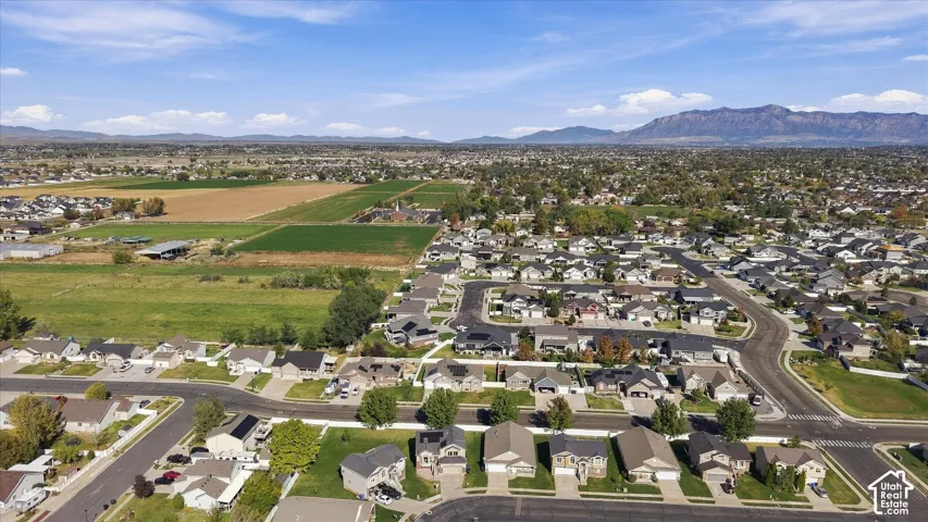 Aerial perspective of a residential neighborhood featuring asphalt paved streets, single-family residential dwellings, surrounding agricultural fields, and a distant mountain backdrop