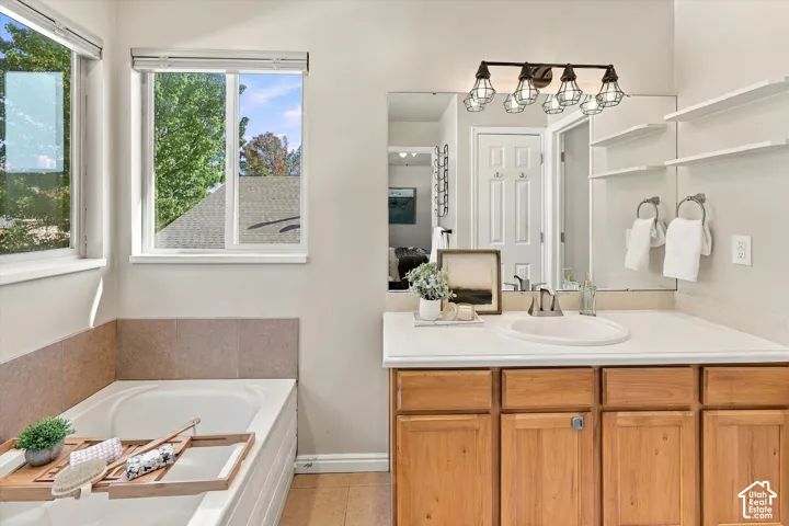 Bathroom featuring a soaking tub with tile surround, wood-finish vanity cabinetry, solid-surface countertop with integrated sink, wall-to-wall mirror, and multi-light industrial-style fixture