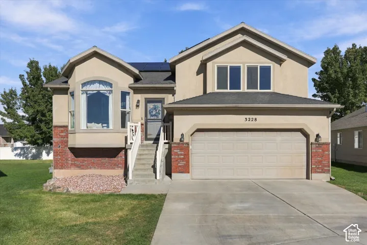 Two-story exterior featuring stucco and brick siding, a concrete driveway, an attached two-car garage, solar panels, and a bay window