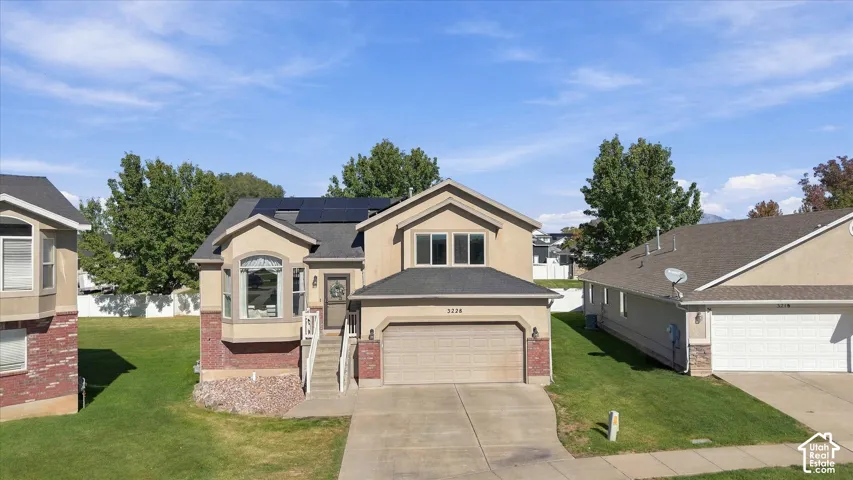 Two-story exterior featuring a stucco and brick facade, an attached two-car garage, integrated solar panels, and a concrete driveway
