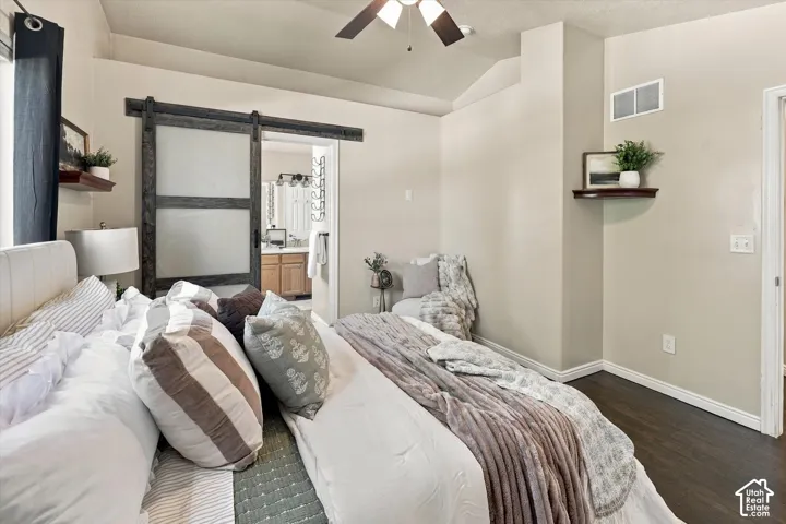 Vaulted ceiling with integrated ceiling fan, dark wood-finish flooring, and frosted glass sliding barn door with dark hardware