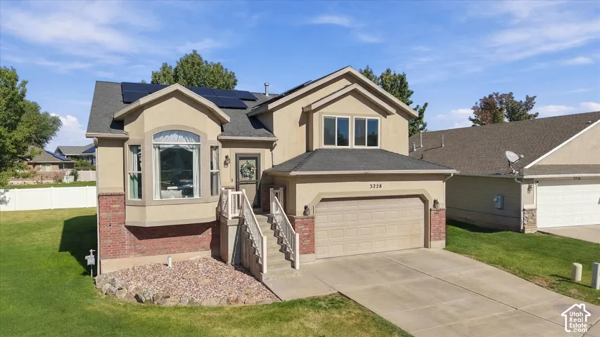 Multi-level exterior featuring tan stucco siding, red brick accents, solar panels, and a two-car garage