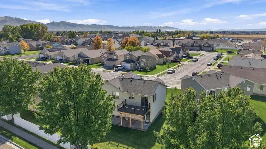 Aerial perspective of a multi-story residence featuring a raised wooden deck with railings, a paved patio area, and a backdrop of mountain scenery