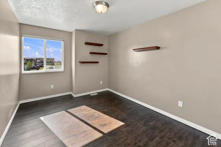 Room featuring dark wood-finish flooring, a single-pane sliding window, and multiple built-in wall-mounted wooden shelves