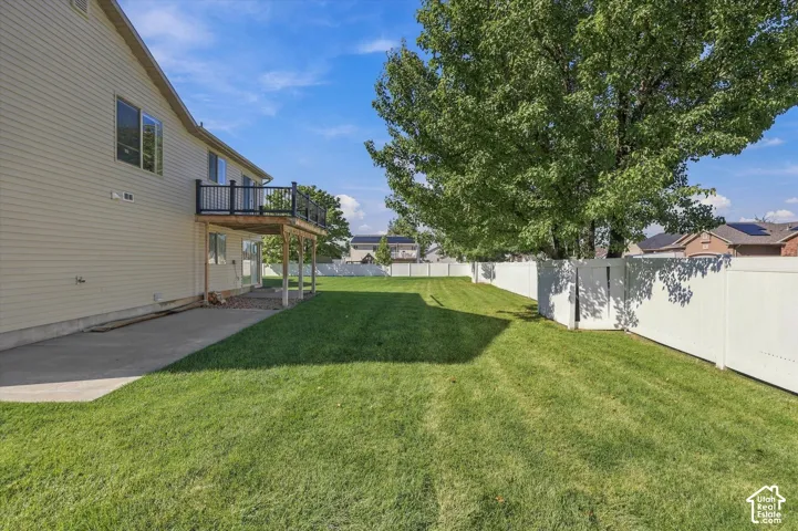 Backyard featuring a concrete patio, an elevated wooden deck with black railings, a full-perimeter white vinyl fence, and established shade trees
