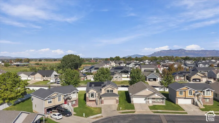 Aerial perspective featuring residential lots with manicured lawns, asphalt driveways, and mountain backdrop
