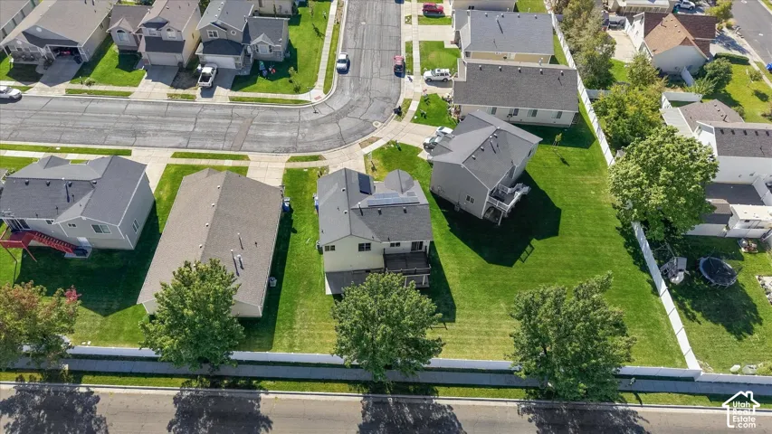 Aerial perspective featuring a residential lot with a multi-level deck, rooftop solar panels, a fenced backyard, and mature trees