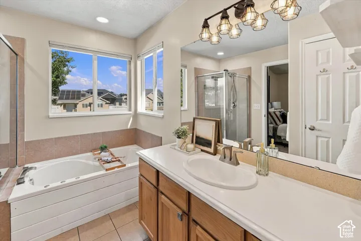 Bathroom featuring a soaking tub, separate glass-enclosed shower, wood-finish cabinetry, countertop with integrated sink, and multi-bulb industrial-style vanity lighting