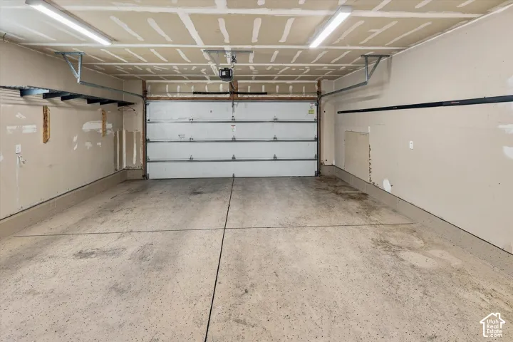 Two-car garage featuring a concrete floor, sectional overhead door, dual linear LED light fixtures, and wall-mounted storage track systems