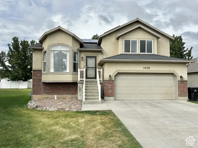 Stucco and brick facade featuring a front-facing bay window, multi-gabled roofline, concrete driveway, and attached two-car garage