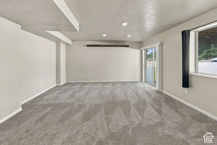 Neutral-toned interior space featuring recessed ceiling lighting, wall-to-wall carpeting, a decorative wood-finish wall beam, and a glass sliding door
