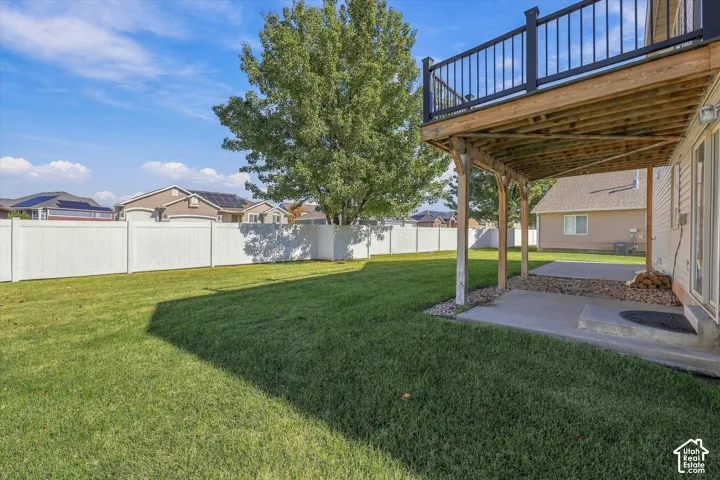 Backyard featuring a grass lawn, white vinyl fencing, a concrete patio, and a raised wooden deck with metal railing