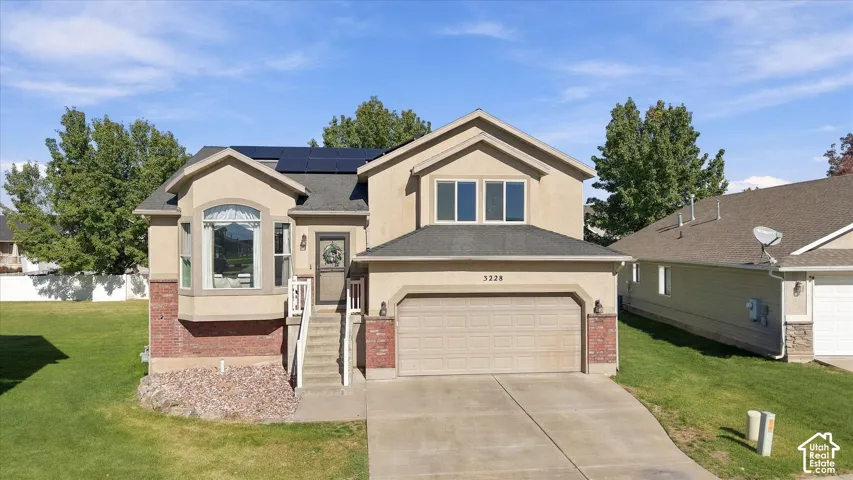 Two-story exterior featuring a brick and stucco facade, an attached two-car garage, roof-mounted solar panels, a concrete driveway, and a front-facing bay window