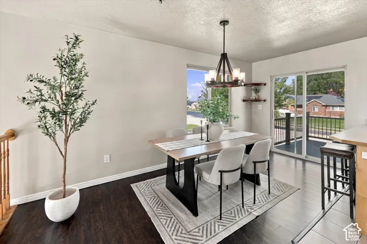 Dark wood-finish flooring, a tiered wheel-style chandelier, sliding glass doors to a balcony, and dual floating corner shelves