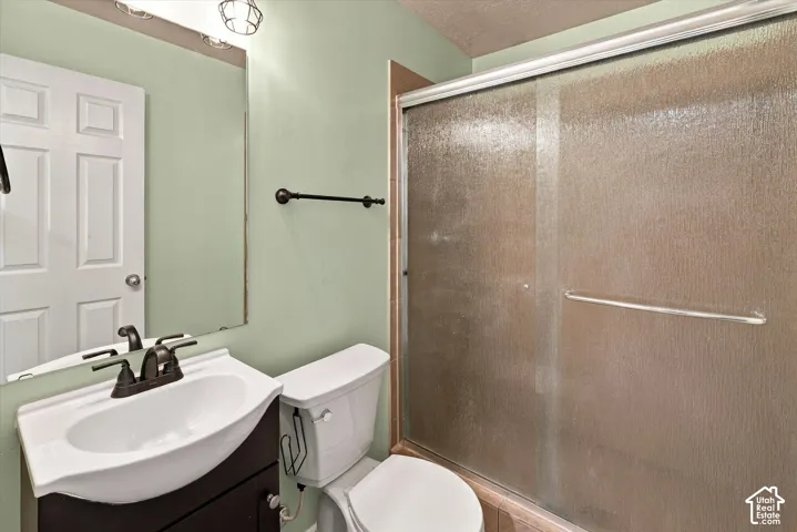 Bathroom featuring a dark-finish vanity with a white basin, dark-finish faucet, wall-mounted mirror, and a walk-in shower with textured glass sliding doors