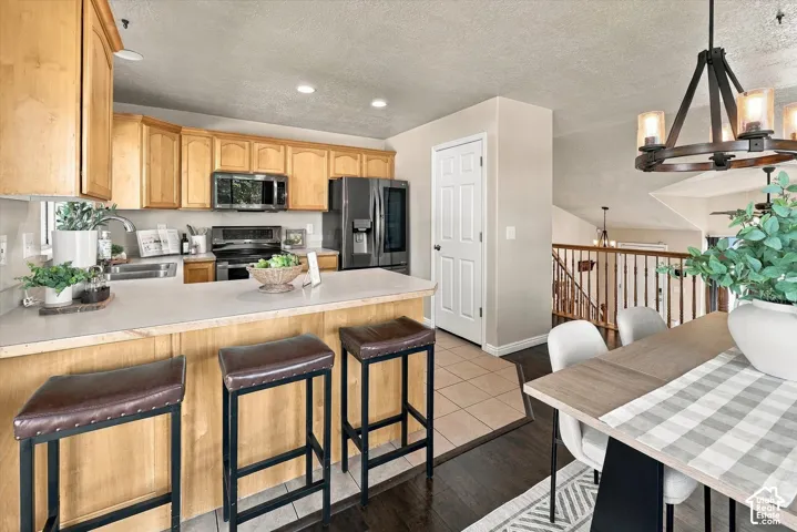 Kitchen featuring light wood cabinetry, stainless steel appliances, solid-surface countertops, tile flooring, and a rustic-style chandelier