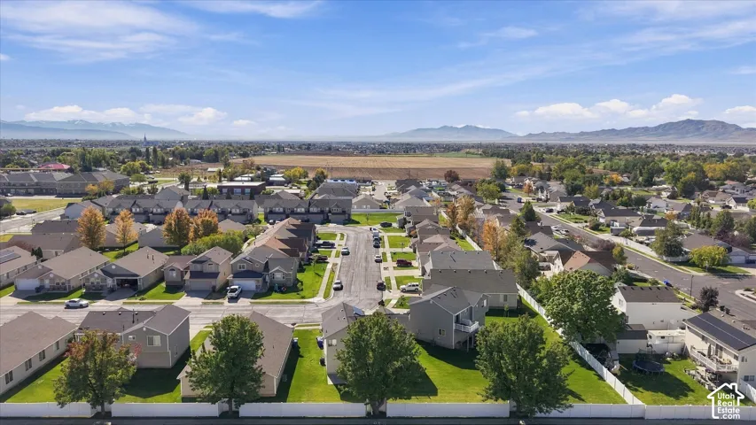 Aerial perspective of a residential neighborhood featuring paved streets, mature deciduous trees, vinyl perimeter fencing, and prominent mountain backdrops