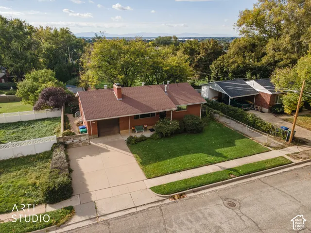 Single-story brick exterior residence featuring a composite shingle roof, attached garage, concrete driveway, and expansive lawn with mature trees