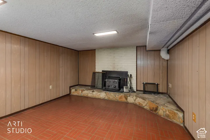 Wood paneling, painted brick fireplace surround, raised stone hearth, and terracotta-style tile flooring