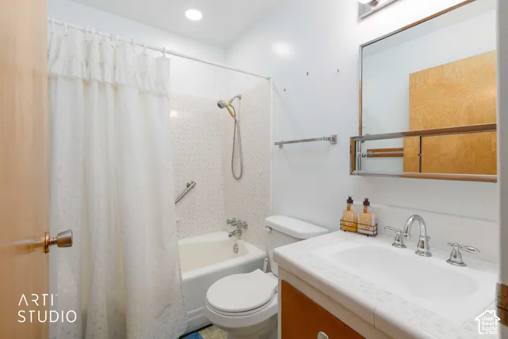 Bathroom featuring a tiled vanity countertop, wood-toned cabinetry, a framed wall-mounted mirror, and a tub-shower combination with a metal grab bar