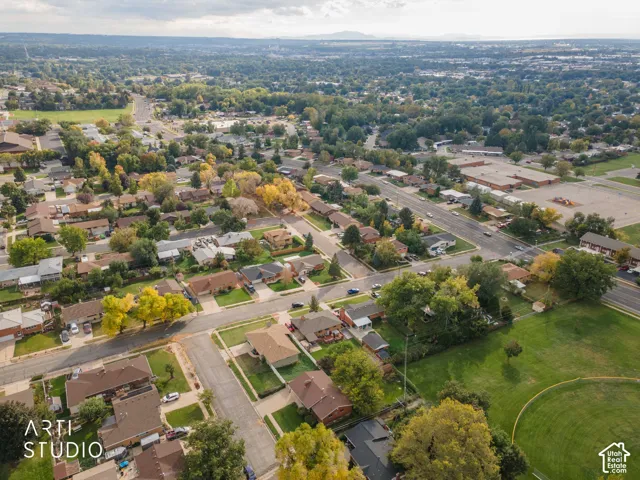 Aerial perspective featuring a grid of residential streets, mature deciduous trees, and an open grass field