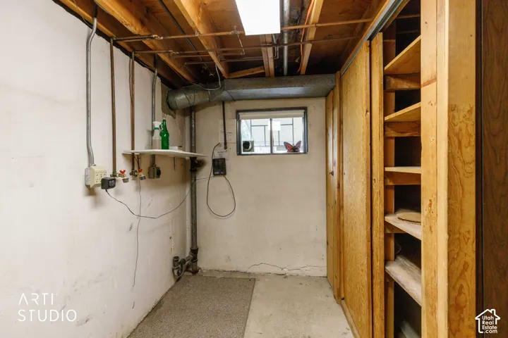 Utility area featuring exposed ceiling joists, concrete flooring, built-in wooden shelving, and wall-mounted plumbing connections