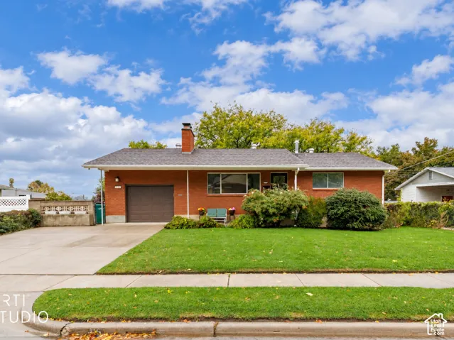 Red brick exterior featuring an attached one-car garage, a central masonry chimney, and a concrete driveway