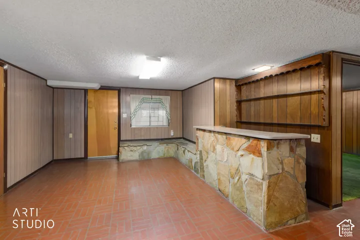 Rec room featuring wood-paneled walls, a built-in bar with natural stone facing, integrated shelving, and ceramic tile flooring