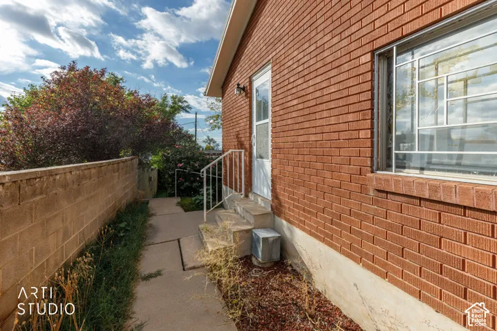 Red brick exterior featuring concrete steps with a metal handrail, a concrete walkway, and a masonry retaining wall