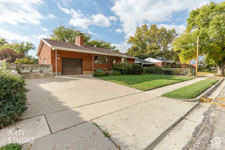 Single-story brick exterior featuring a concrete driveway, attached garage, stone retaining wall, and front lawn