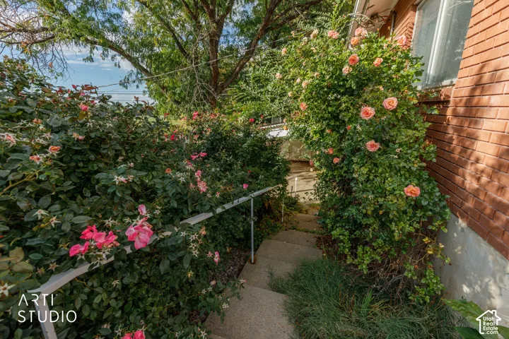 Exterior staircase featuring brick siding, metal handrailing, and established rose bushes