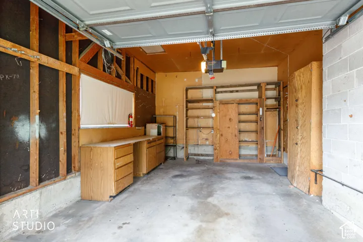 Garage interior featuring a concrete floor, exposed wood stud framing, built-in wooden cabinetry, custom shelving units, and a window with a roller shade