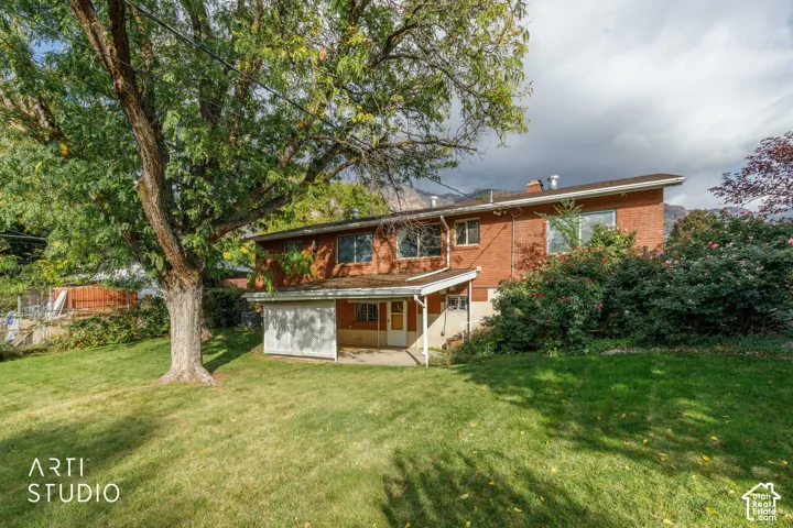 Red brick exterior featuring a covered patio, expansive lawn, mature shade trees, and mountain backdrop