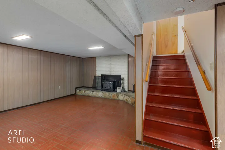 Finished space featuring wood-paneled walls, a brick fireplace with a stone hearth, tile flooring, and a staircase with wooden handrails