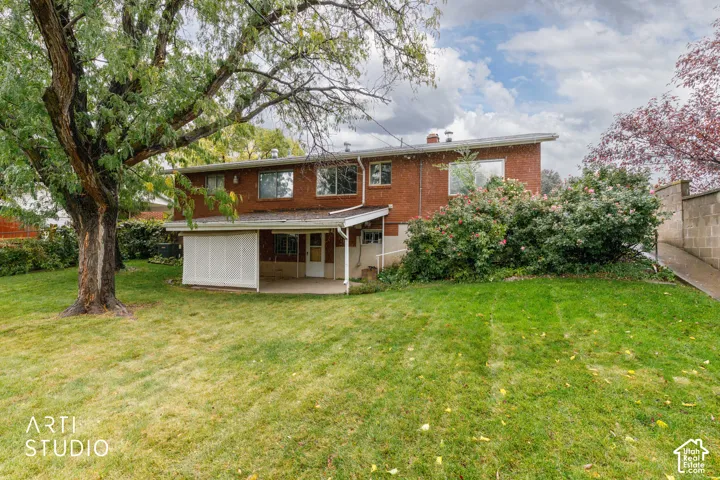 Brick exterior featuring a covered patio, expansive lawn, mature shade tree, and established landscaping