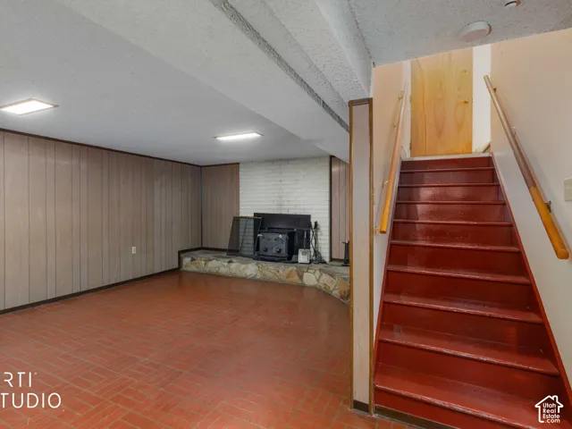 Finished space featuring wood-paneled walls, a brick fireplace with a stone hearth, tile flooring, and a staircase with wooden handrails