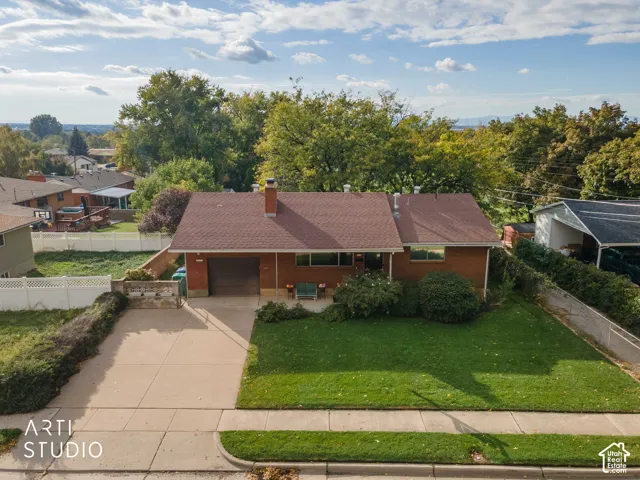 Rambler-style exterior featuring brick masonry, an attached garage, concrete driveway, and a front lawn with mature landscaping