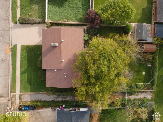 Aerial view featuring a paved driveway, a gabled roof with chimney, and a fenced-in yard with mature trees