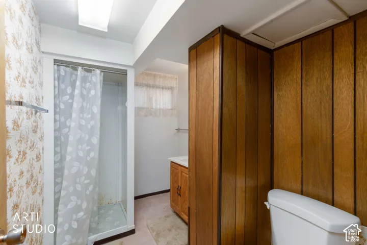 Stall shower with a framed glass door, wood-paneled accent walls, vanity cabinet with a sink, and integrated overhead lighting