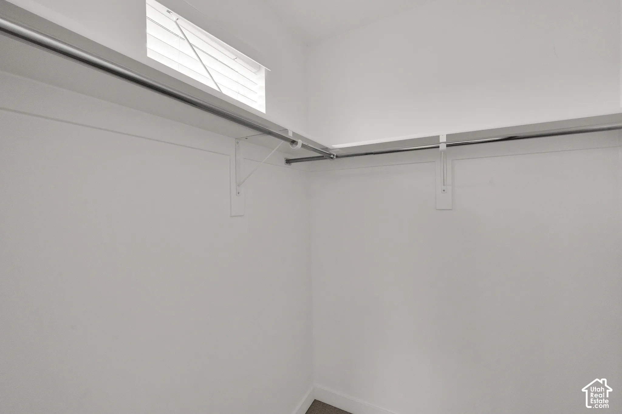 Storage area featuring wrap-around shelving, dual metal garment rods, and a transom window with integrated blinds
