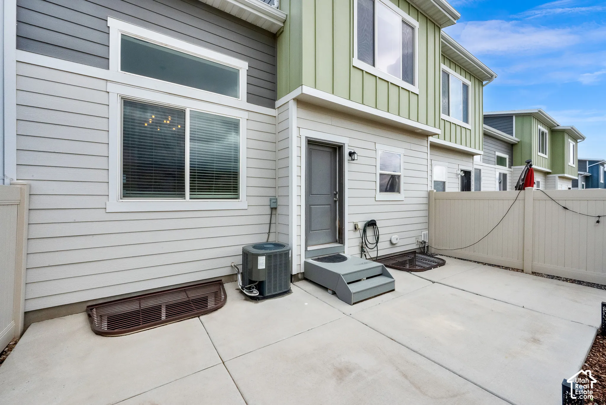 Multi-level exterior featuring horizontal lap and vertical board-and-batten siding, concrete patio, privacy fencing, and window wells