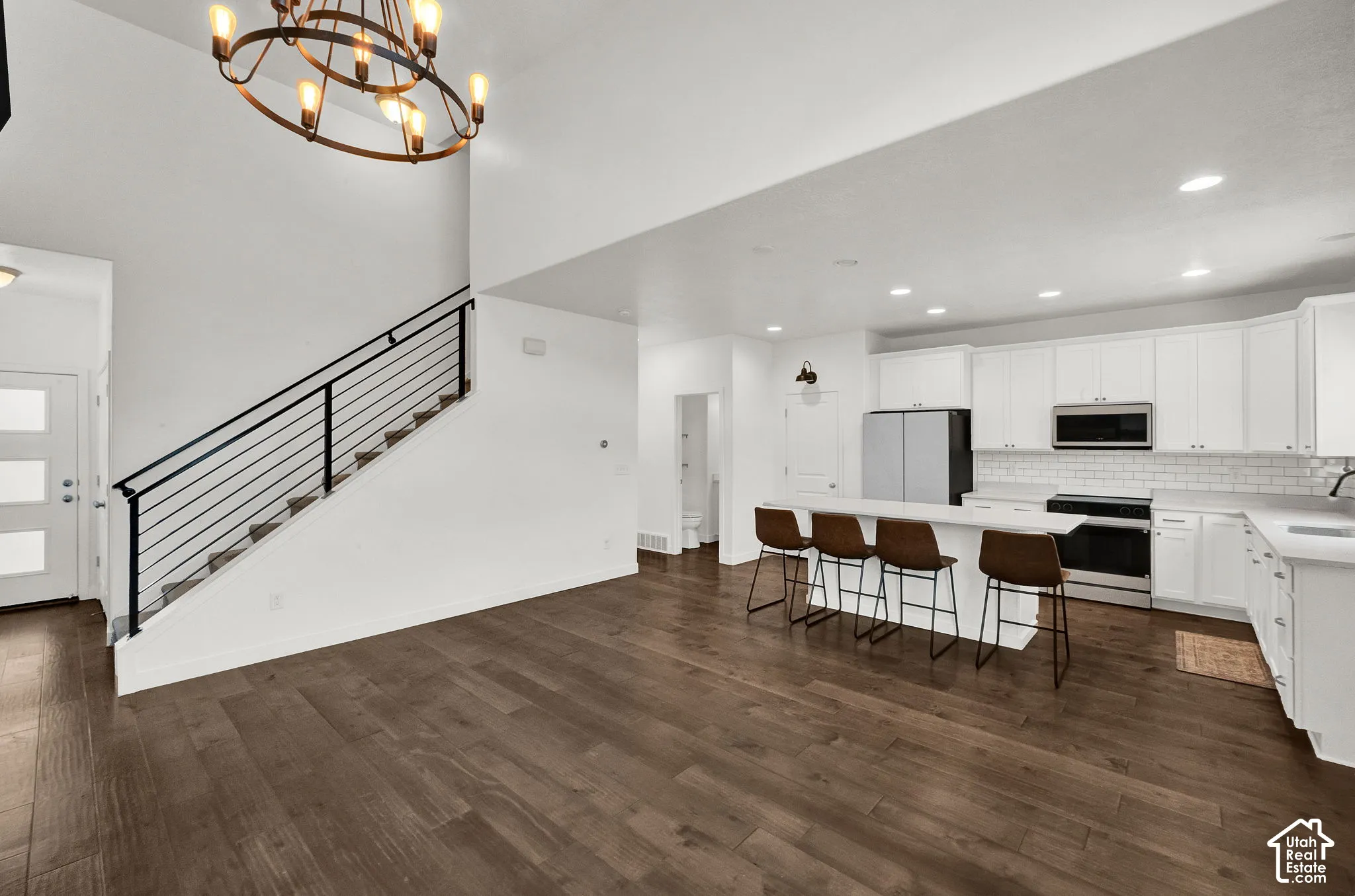 Open-concept interior featuring wood-finish flooring, white cabinetry, a large kitchen island, recessed lighting, and a staircase with a metal railing