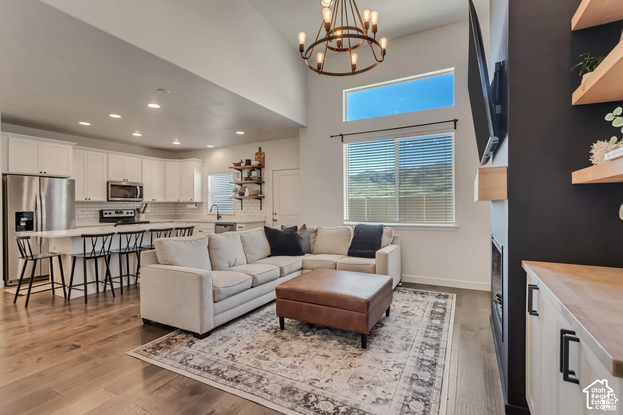 Vaulted ceiling with a chandelier, wood-finish flooring, white kitchen cabinetry with stainless steel appliances, and a built-in fireplace