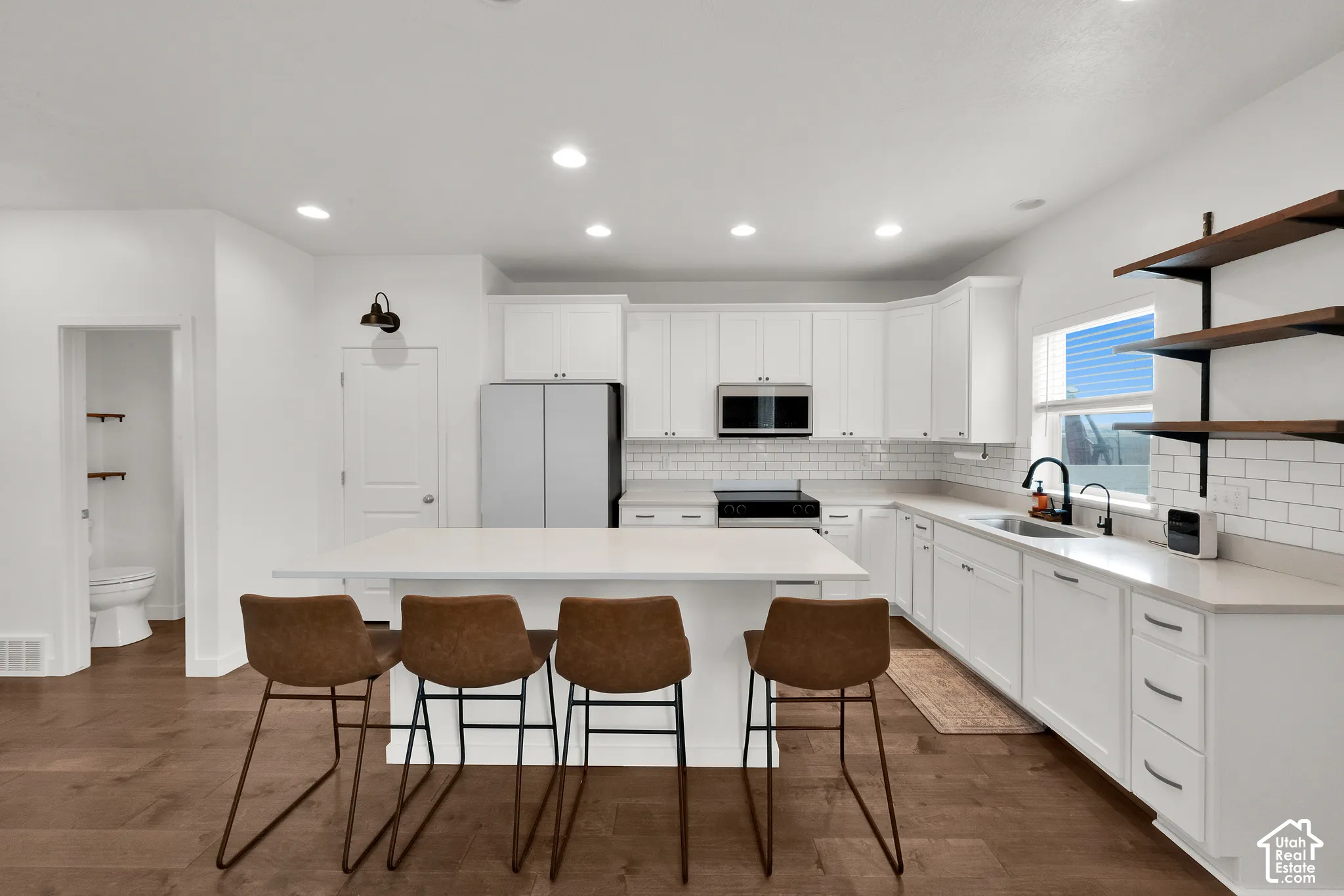 Kitchen featuring white cabinetry, quartz countertops, subway tile backsplash, wood-finish flooring, and open shelving