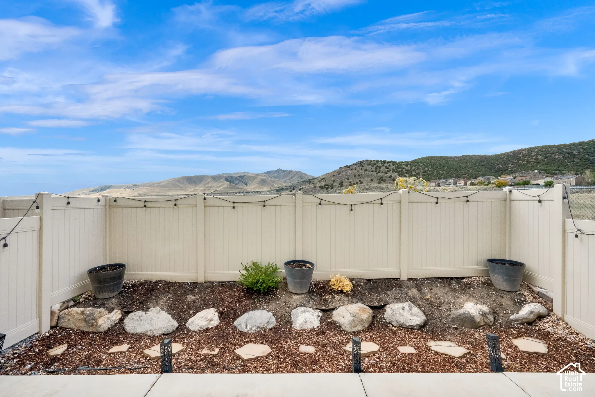 Backyard space featuring a light-colored privacy fence, stone-lined garden bed, concrete patio, and mountain backdrop