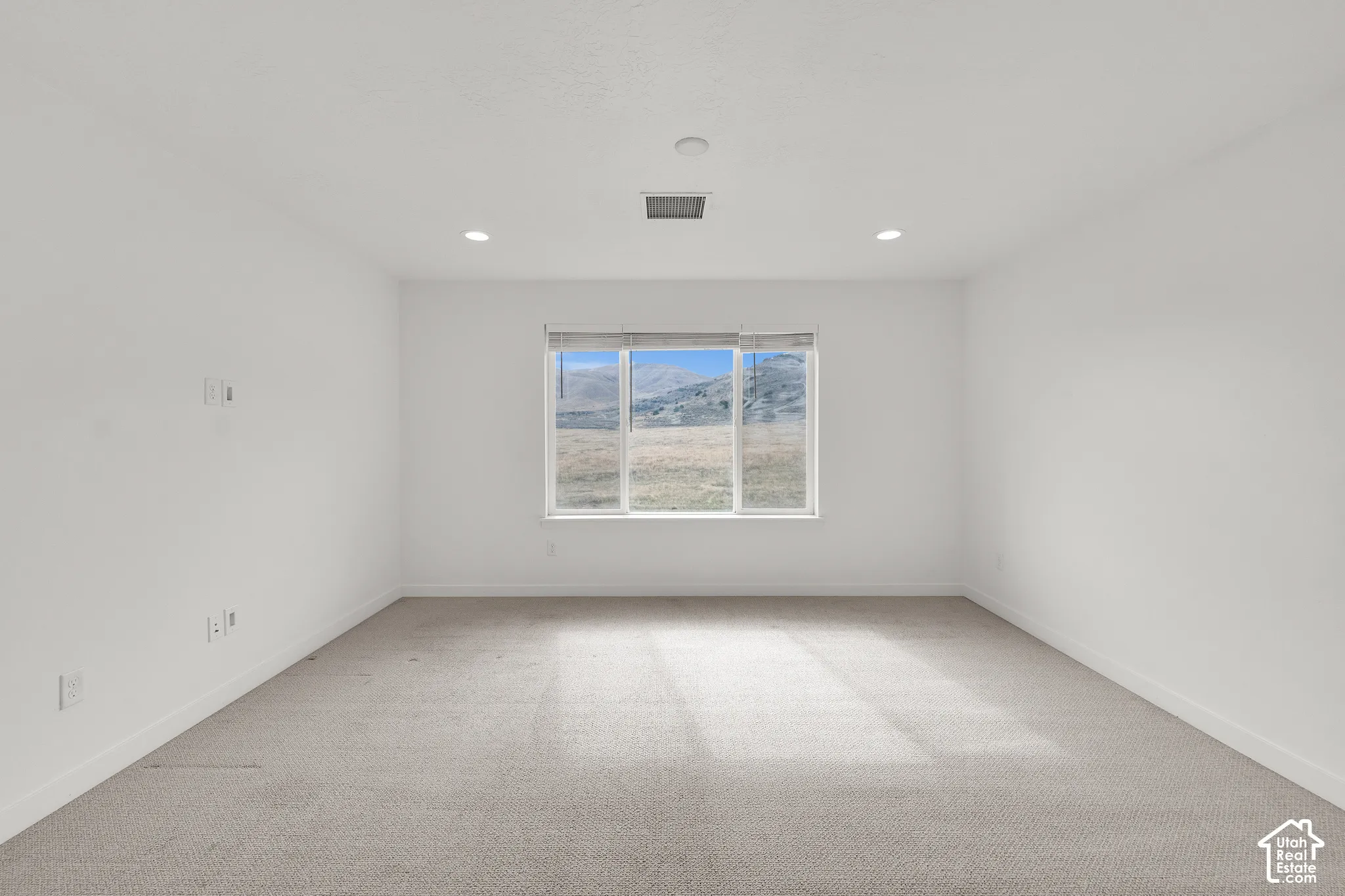 Neutral-toned interior space featuring wall-to-wall carpeting, recessed ceiling lighting, and a large picture window showcasing a mountain landscape