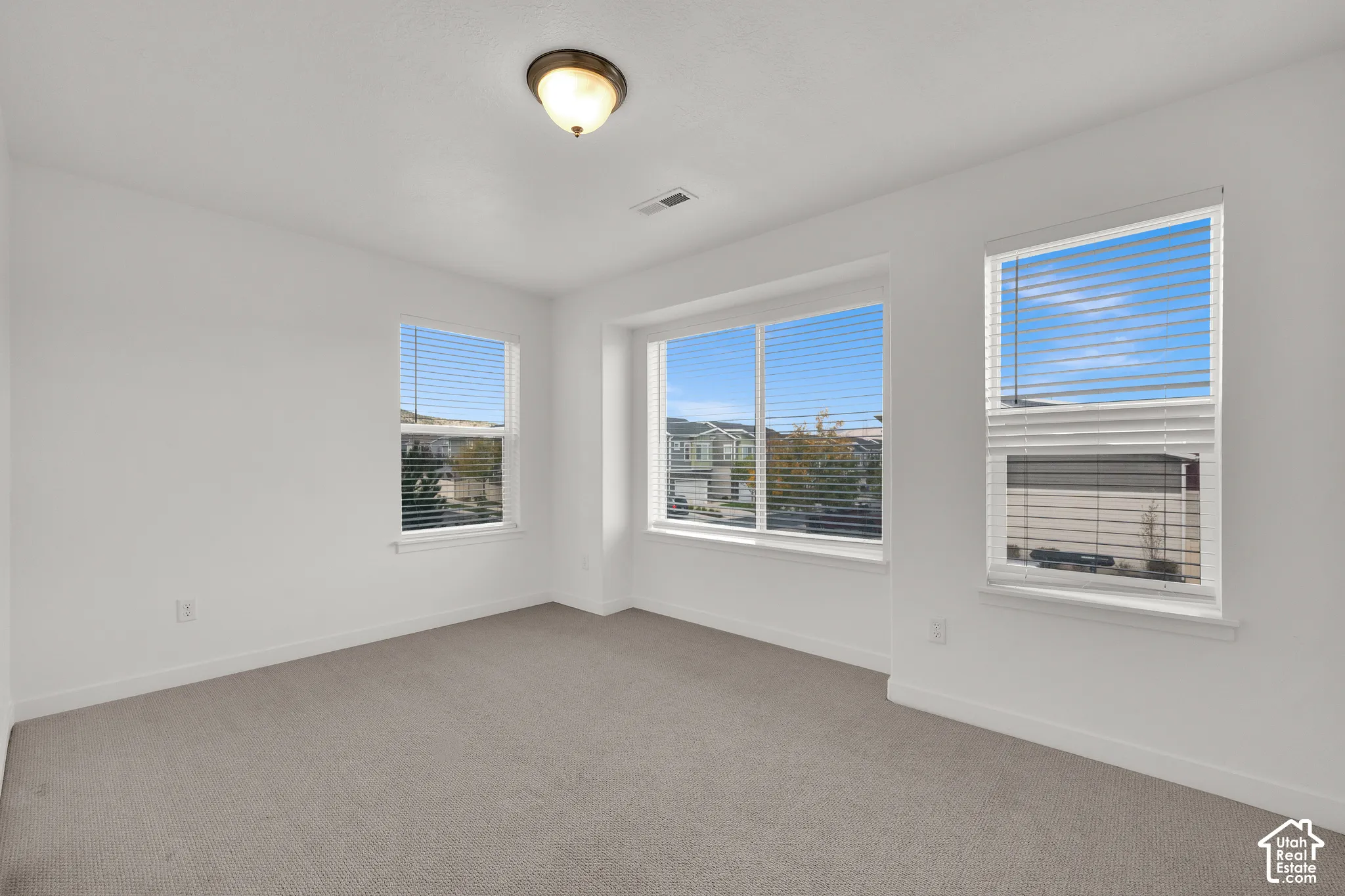 Neutral interior space featuring high-contrast walls, neutral-toned carpeting, triple-pane window configuration, and a flush-mount overhead light fixture