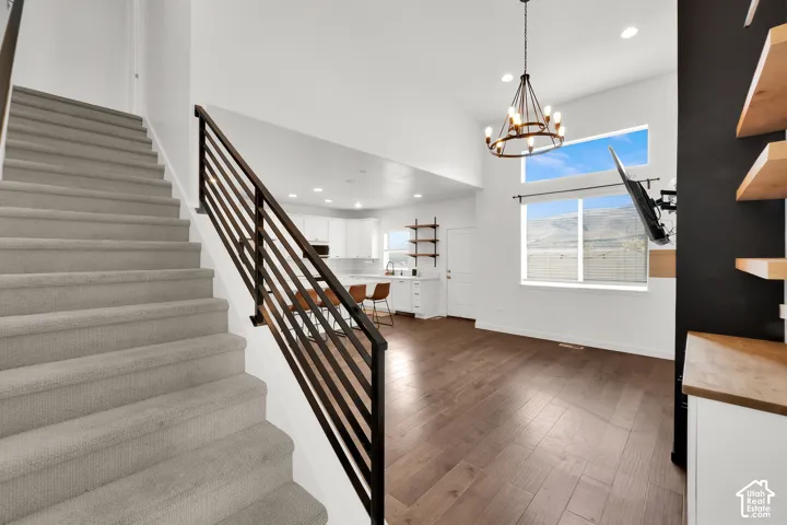 High-ceilinged common area featuring wood-finish flooring, a metal horizontal-slat staircase railing, a multi-light chandelier, and built-in wood shelving
