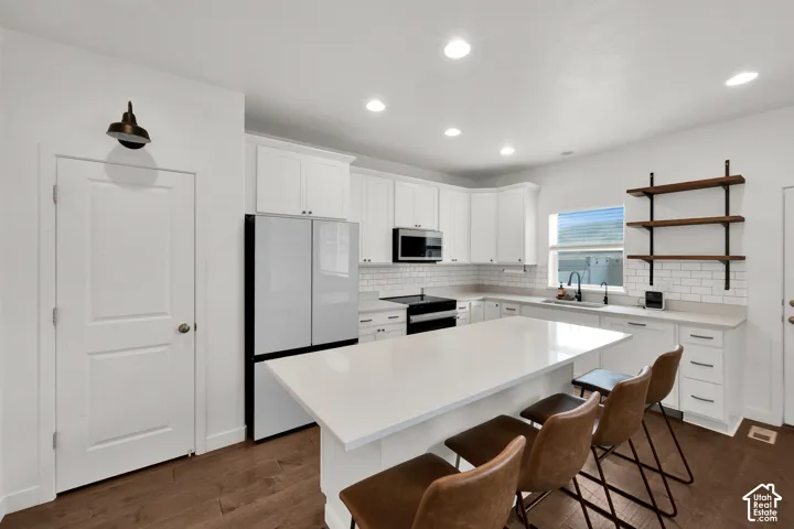 Kitchen featuring white shaker-style cabinetry, quartz countertops, subway tile backsplash, wood-finish flooring, and industrial-style wall-mounted shelving